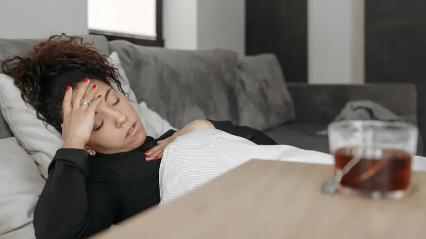 une femme est allongée sur un canapé, ferme les yeux et a une main posée sur sa tête.