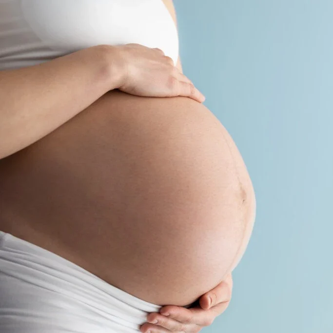 un ventre de femme enceinte de profil avec une main au dessus et une en dessous