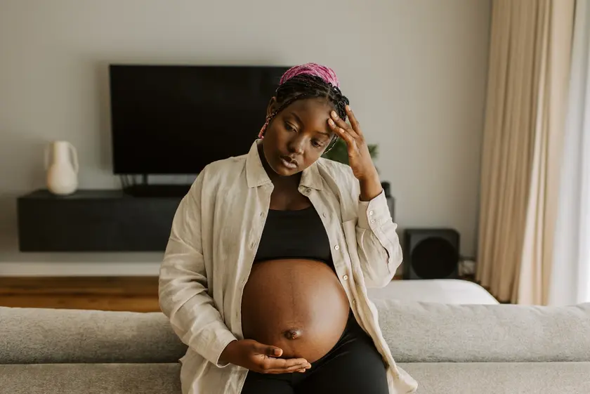 une femme enceinte a mal à la tête, elle se tient le ventre et la tête
