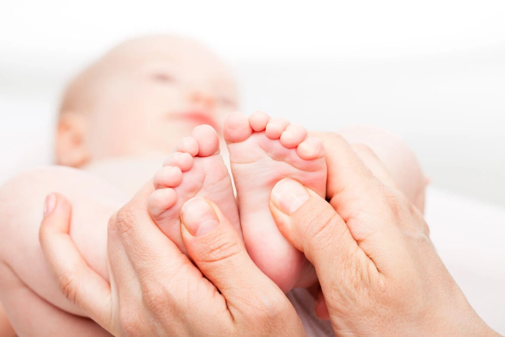 réflexologie pédiatrique deux pied de bébés sont tenus dans des mains adultes.