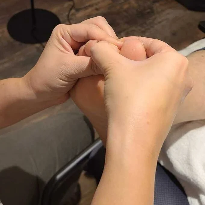 pratique reflexologie plantaire deux mains effectuent des pressions sur un pied entre le gros orteil et les autres.