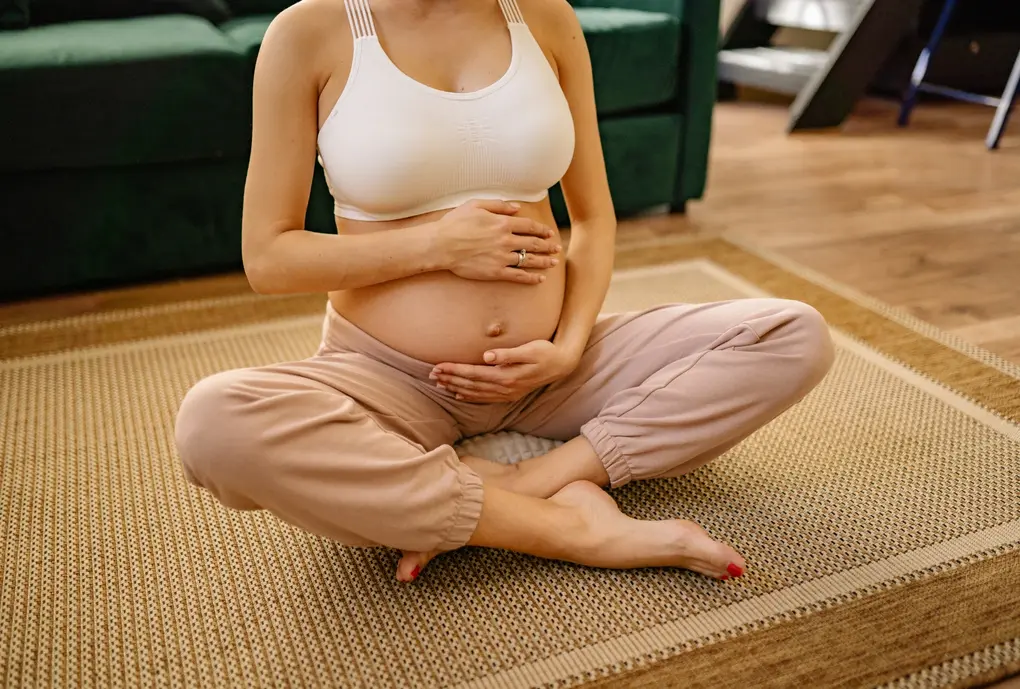 relaxation femme enceinte une femme enceinte est assise en tailleur dans un salon avec ses mains sur sont ventre